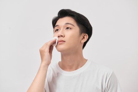 Beauty portrait of confident young man using cotton pad on his face isolated over white backgroundの写真素材