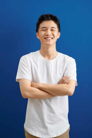 Smiling handsome man in t-shirt standing with crossed arms isolated on blue backgroundの写真素材