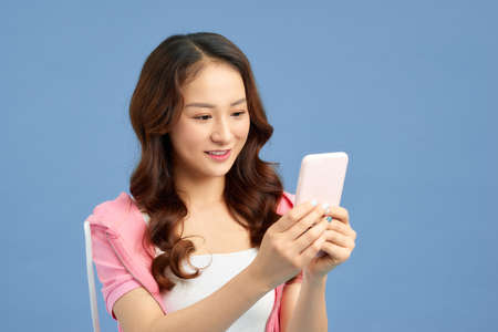 Happy young Asian woman texting message with her smartphone isolated blue background.の写真素材
