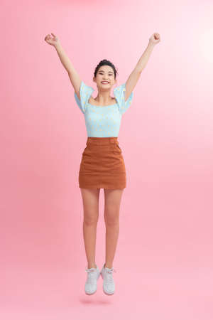 Full length portrait of a joyful young woman jumping and celebrating over pink background