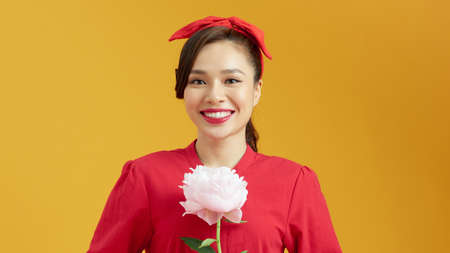 Pretty girl holding a peony on yellow background