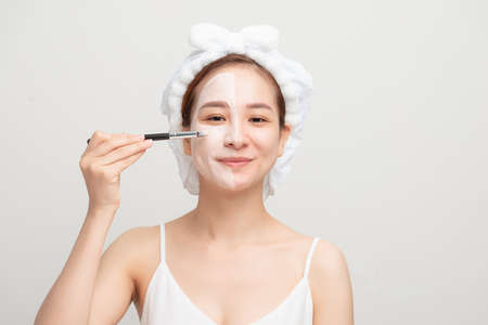 Woman with lifting cream applied on a half of her face, isolated on whiteの写真素材