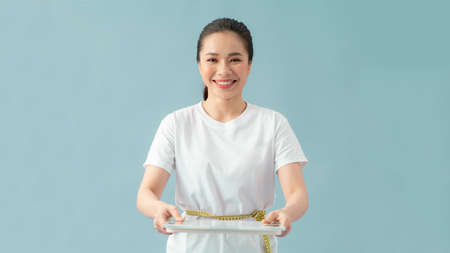 Asian beautiful woman are using the measuring tape to measure around the waist and holding  weight scale on blue backgroundの写真素材