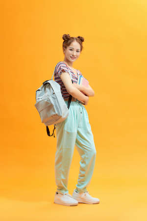 Full length portrait of a cute smiling girl holding books isolated on the yellow backgroundの写真素材