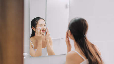 Portrait of beautiful young woman washing her face in a home bathroom.の写真素材