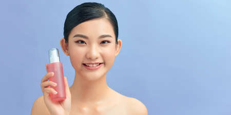 Smiling young girl demonstrates moisturizing tonic in pink bottle.の写真素材