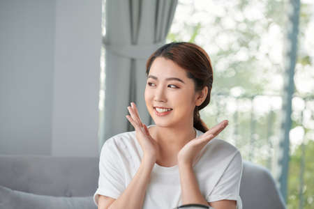 Beautiful young woman is touching her face and smiling while looking at the mirrorの写真素材