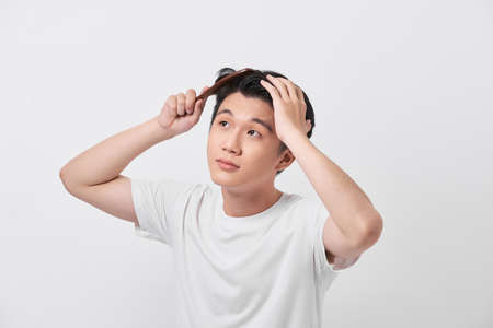 people concept - smiling young man brushing hair with comb on white backgroundの写真素材