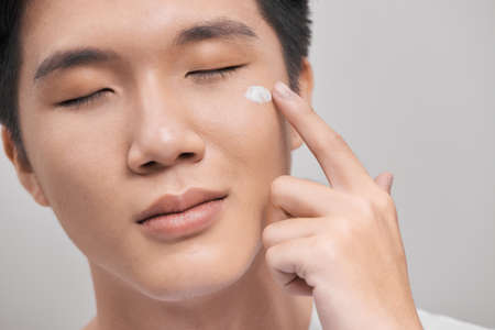 smiling man applying cream lotion on faceの写真素材