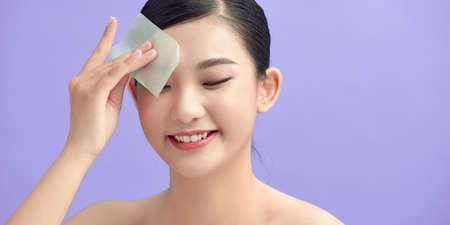 Woman using facial oil blotting paper, beauty product at studioの写真素材