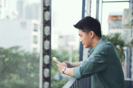 Happy man using mobile phone at balconyの写真素材