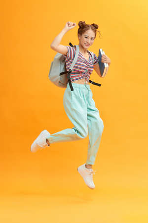 Casual female student running. isolated on yellow backgroundの写真素材
