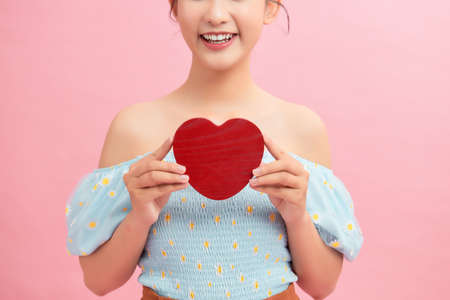 Waist-up portrait of pretty Asian woman looking away with toothy smile while holding Valentines Day card in handsの写真素材