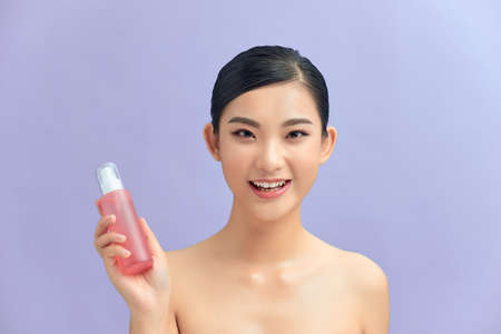 Beauty portrait of pretty young topless woman showing cosmetic skin oil in bottle isolated over purple backgroundの写真素材