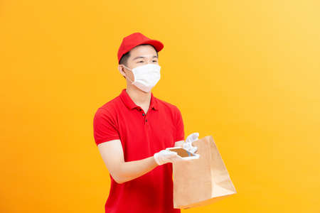 Young delivery man in medical gloves and protective face mask holding smart phone with copy space and shopping bags in hands.の写真素材