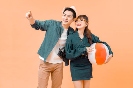 Pretty girl holding inflatable ball near handsome man holding digital camera on yellow backgroundの写真素材