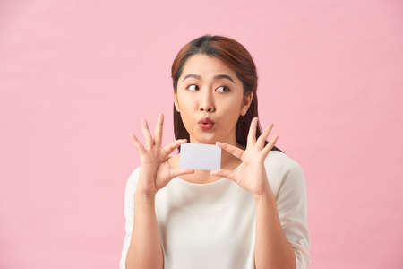 Happy excited amazed young woman holding credit card in hands and looking directly at camera