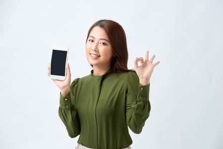 Young beautiful woman holding smartphone showing screen doing ok sign with fingers, smiling friendly gesturing excellent symbolの写真素材
