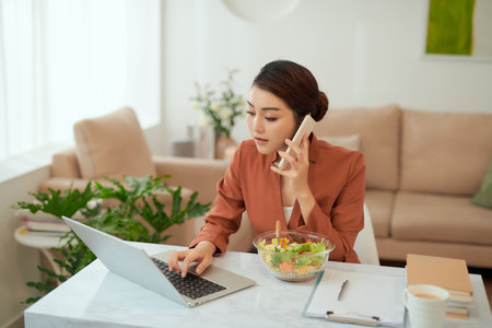 Pretty woman smiling while working from home, on the phone with a saladの写真素材