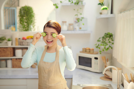 Young housewife playing with food cut slices of sweet cucumber while cooking in the kitchen.の写真素材
