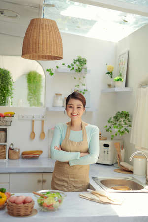 Portrait of smiling woman standing on kitchen. Lady in apron smiling at camera.の写真素材