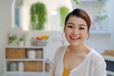 Portrait of young smiling woman sitting against home kitchen backgroundの写真素材