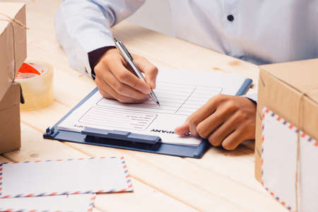 Courier hands writing on cardboard box at table