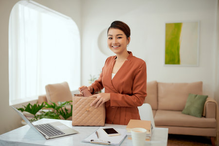 Smiling beautiful young business woman holding one open pink leather handbag putting water bottle insideの写真素材