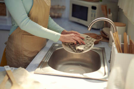 Kitchen porter cleaning white plates in sink in professional kitchen