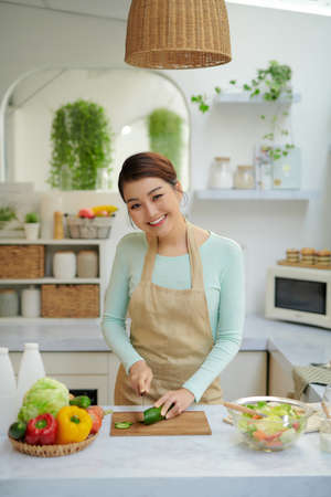 Smiling woman cutting a cucumber in her kitchenの写真素材