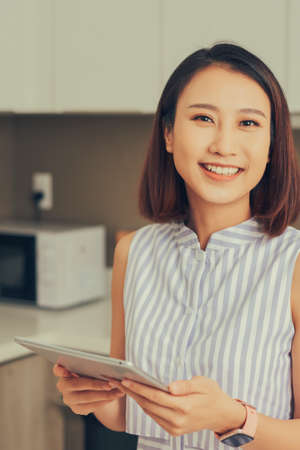 Asian woman using tablet to find recipe making smoothie with fruit and vegetable in kitchen.