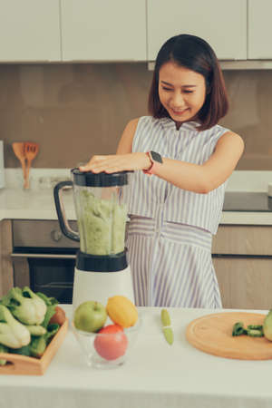 Beautiful Asian Woman juicing making green juice with juice machine in home kitchen. Healthy concept.の写真素材