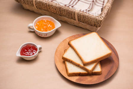 Toast with strawberry and orange jam on a plate on table.