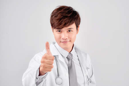 Positive asian male doctor in lab coat showing thumb up gesture over white backgroundの写真素材