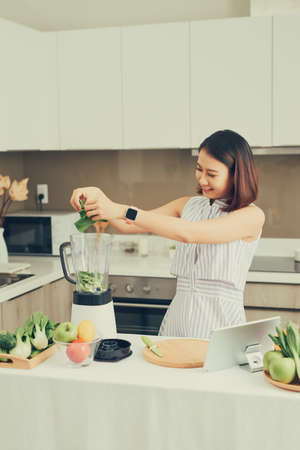 Healthy Asian woman enjoy making green vegetables detox cleanse and green fruit smoothie with...
