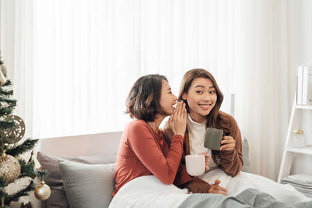 happy friends talking and drinking coffee and tea sitting on a couch at home and gossipingの写真素材