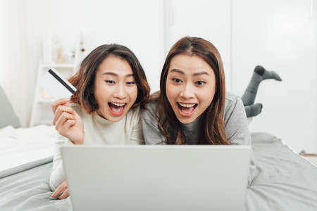 Asian woman friends sitting in living room using digital tablet for online shopping with credit card togetherの写真素材