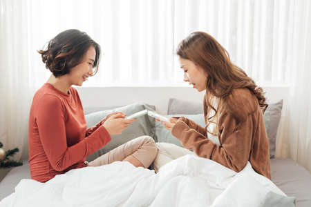 Young happy lesbian lgbtq couple or friends holding smartphone using mobile phone at homeの写真素材