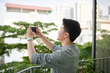 Adult man standing taking photos of beautiful scenery from the balcony of the apartment.