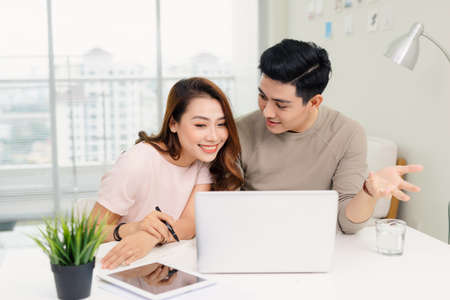 Positive hipster couple having fun while working together remotely at home using modern technologyの写真素材