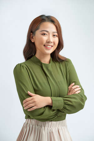 Beautiful young woman in smart casual wear keeping arms crossed and smiling while standing against grey backgroundの写真素材