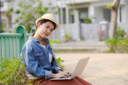 Young woman with laptop sits on couch in the park on a sunny day.の写真素材