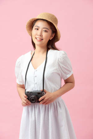 Vertical image of a young woman photographing somebody against a pink backgroundの写真素材
