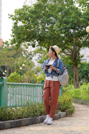 Young beautiful Asian backpack traveler woman using digital compact camera and smile, looking at copy spaceの写真素材