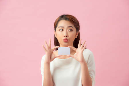 Young Asian beautiful woman holding blank card isolated on pink backgroundの写真素材