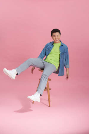 young man sitting on high wooden stool on pink backgroundの写真素材