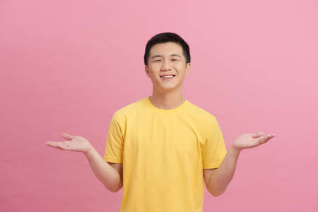 Smiling excited Asian man with open hand gesture on pink backgroundの写真素材