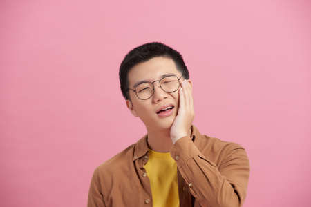 A young and handsome Asian man uses his hand to touch and hold his mouth with painful and suffer face from toothache.の写真素材