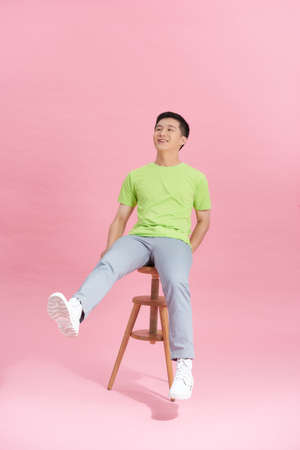 young man sitting on high wooden stool on pink backgroundの写真素材