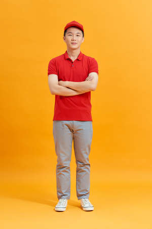 Deliveryman with arms crossed in studio. looking at camera. Full length portrait. isolated gray backgroundの写真素材